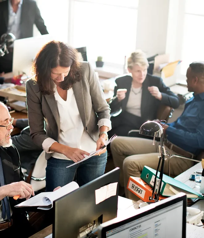 Several people in an office building are arranged in separate groups, each talking about business or discussing paperwork