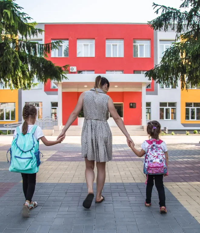 Two students hold hands with their mom as they walk to elementary school.