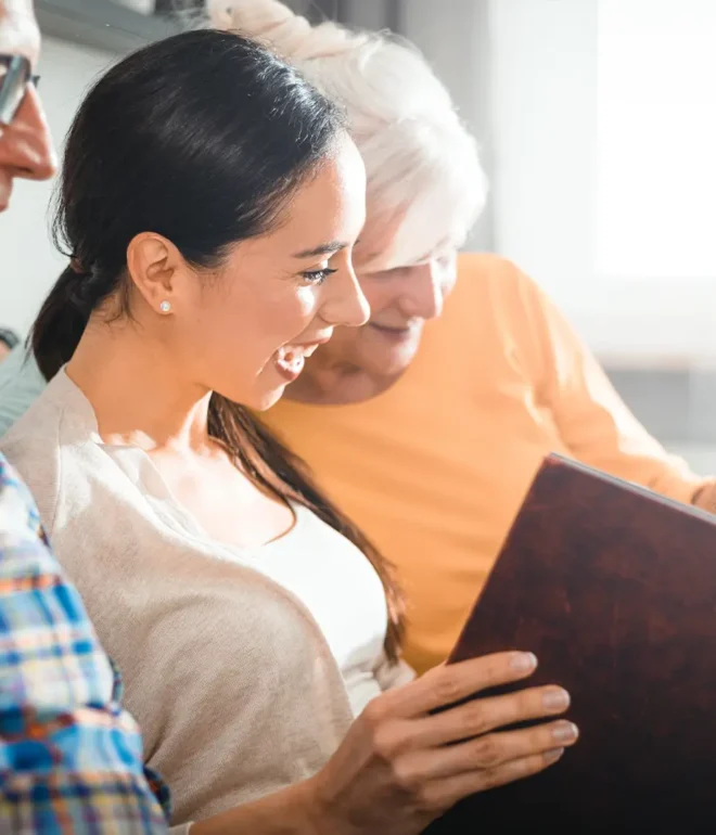 Two grandparents sit with their granddaughter as they look at a family photo album.