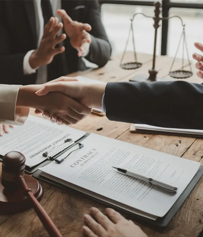 A close-up of two attorneys shaking hands over top of a signed contract document.