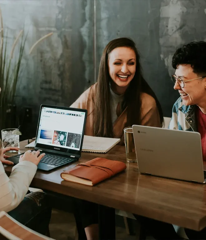 Three smiling young businesspeople sitting at a table and working on computers