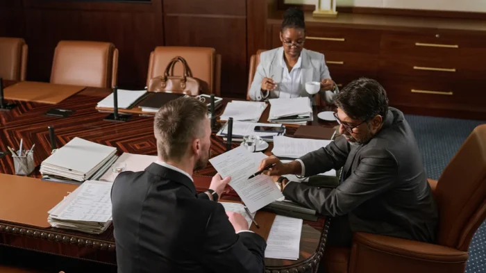Two attorneys and a client in a boardroom. One points at a specific line on a legal document to a client.