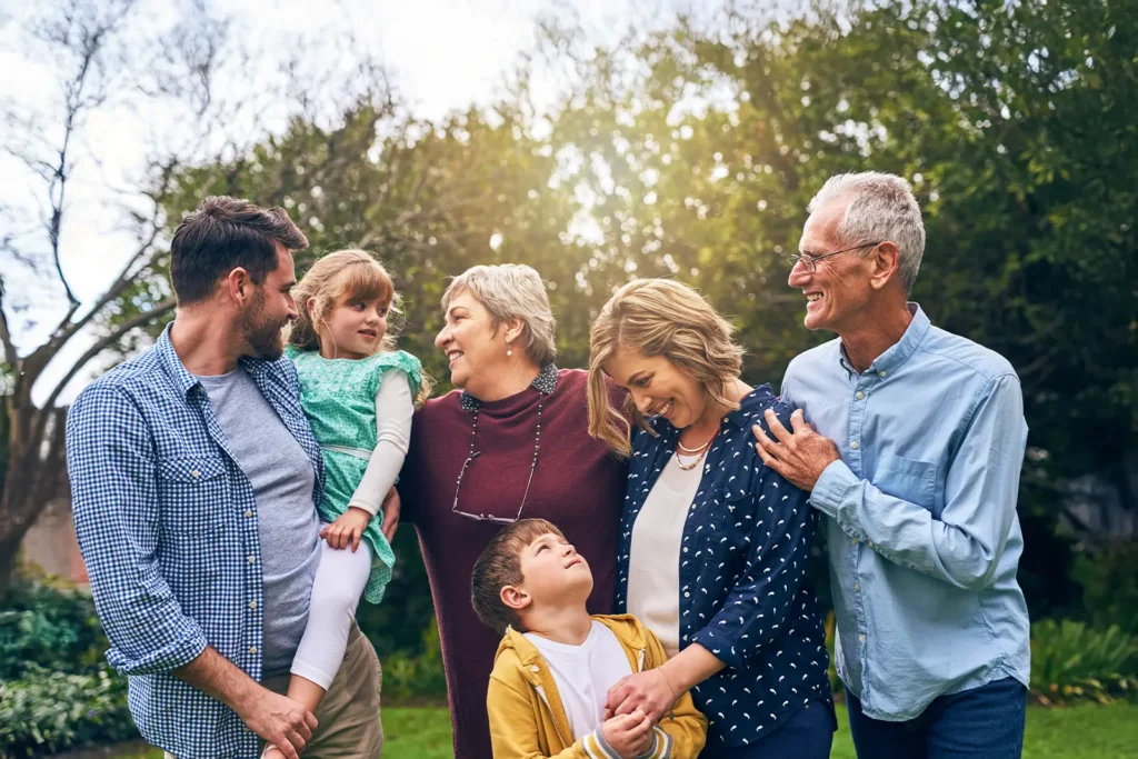 Three generations of a family pose for a photo outdoors, smiling at each other