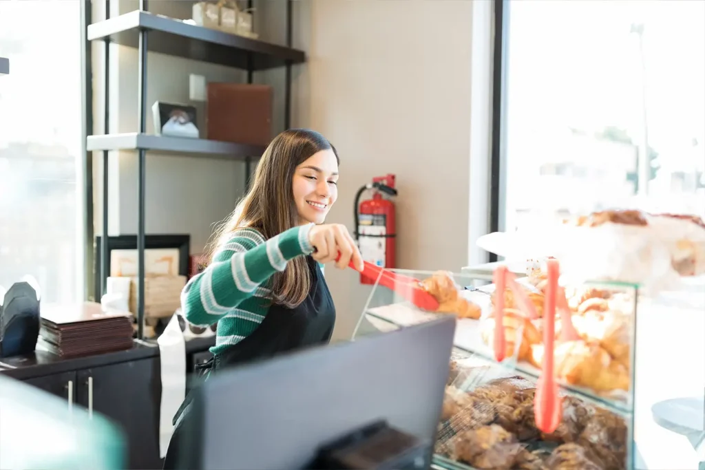 Woman working in a bakery uses tongs to pick up a pastry