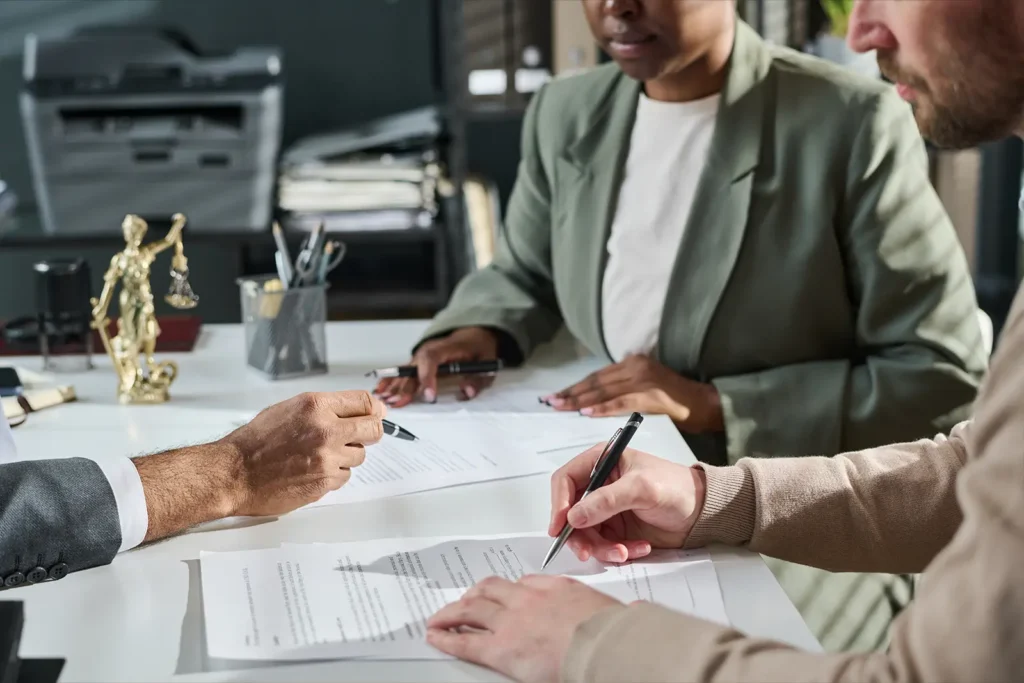 An attorney's hand points at a specific clause with his pen while two clients watch