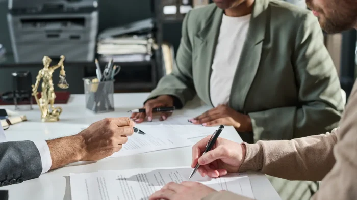 An attorney's hand points at a specific clause with his pen while two clients watch