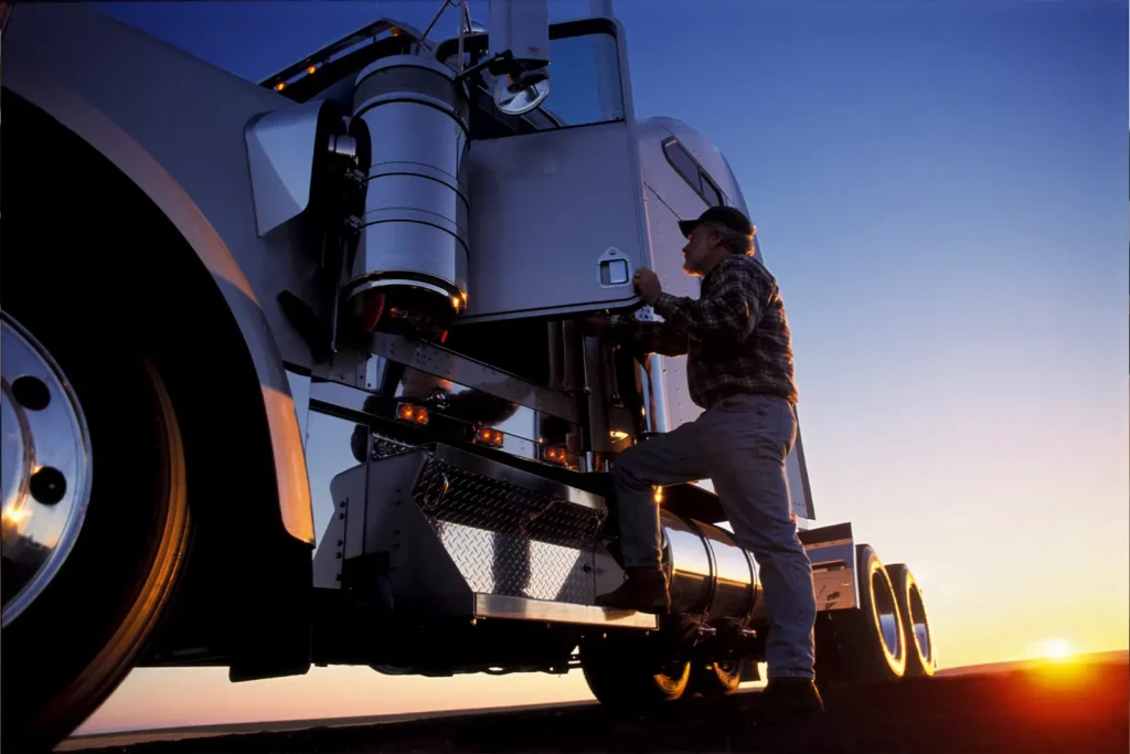 A man enters the driver's side of a big rig truck at sunset.