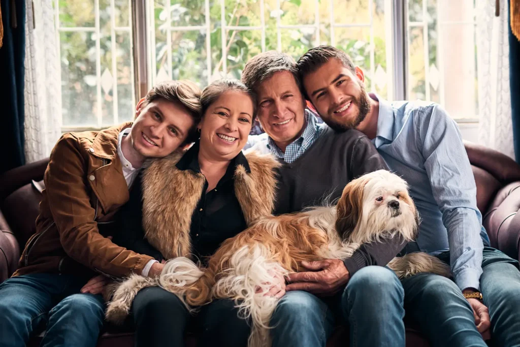 Four family members (mom, dad, and two sons) pose for a photo on their couch. Their dog sits in their laps.