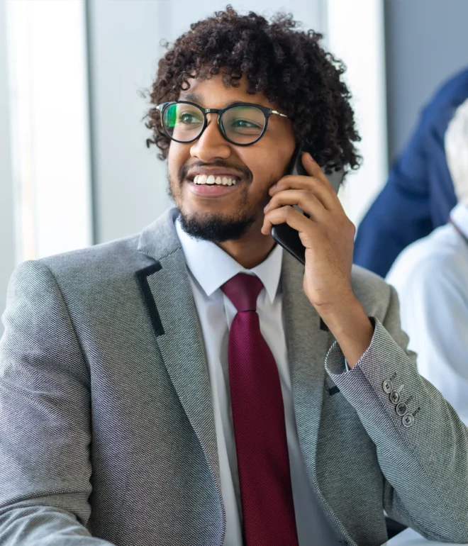 A smiling businessman in suit and tie looks to his left while on a phone call.