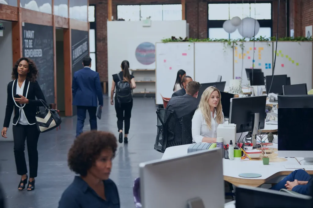 A busy office scene, with workers at computers and walking by
