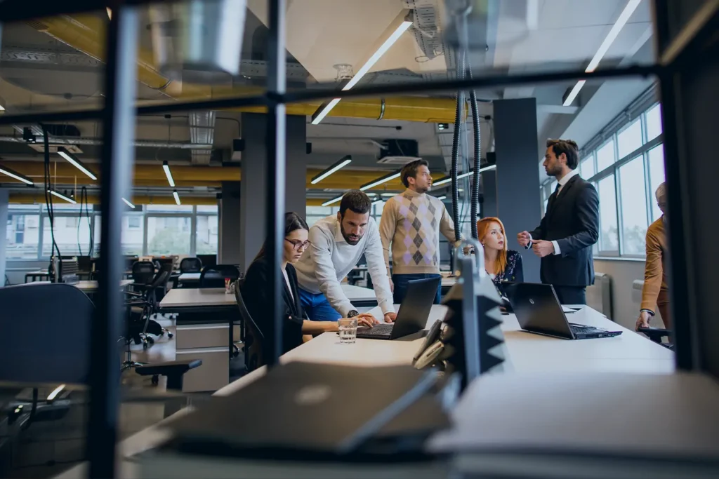 A group of professionals huddle around a computer, discussing their work