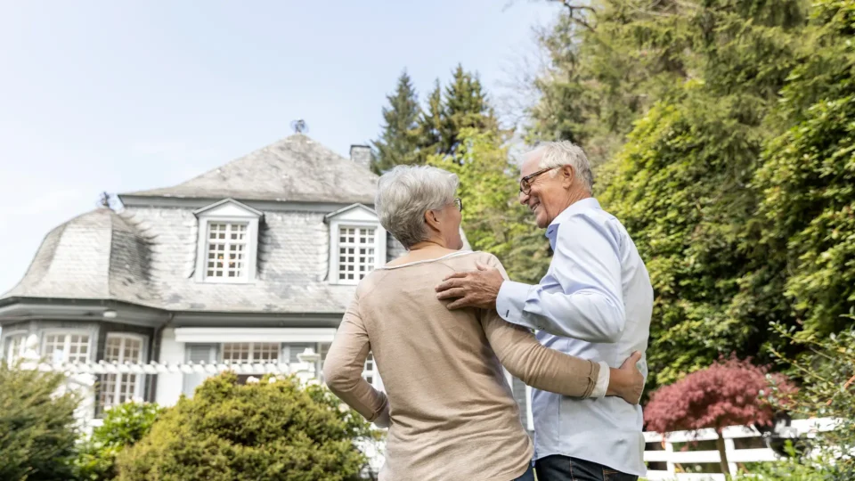 A married couple embraces in front of their home.