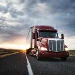 A tractor trailer drives toward the camera at sunset.