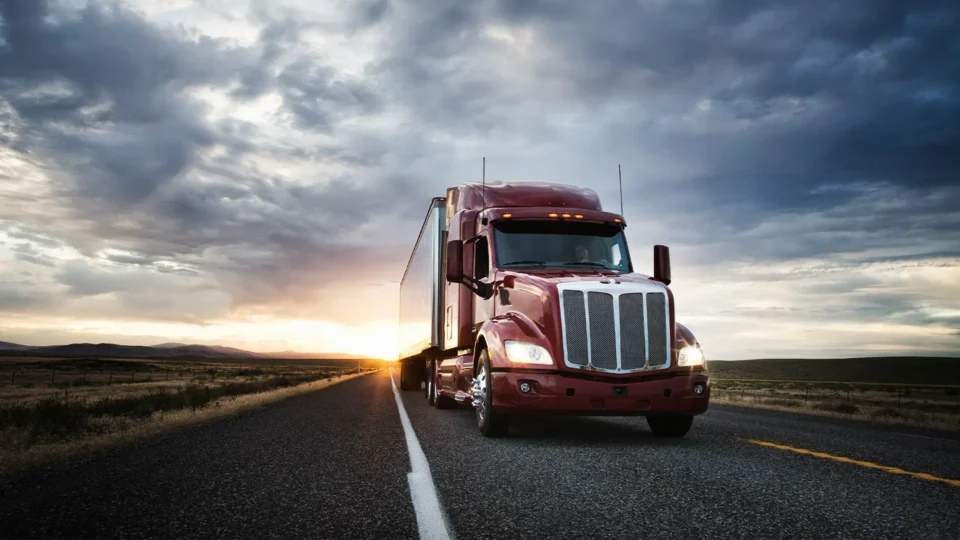 A tractor trailer drives toward the camera at sunset.