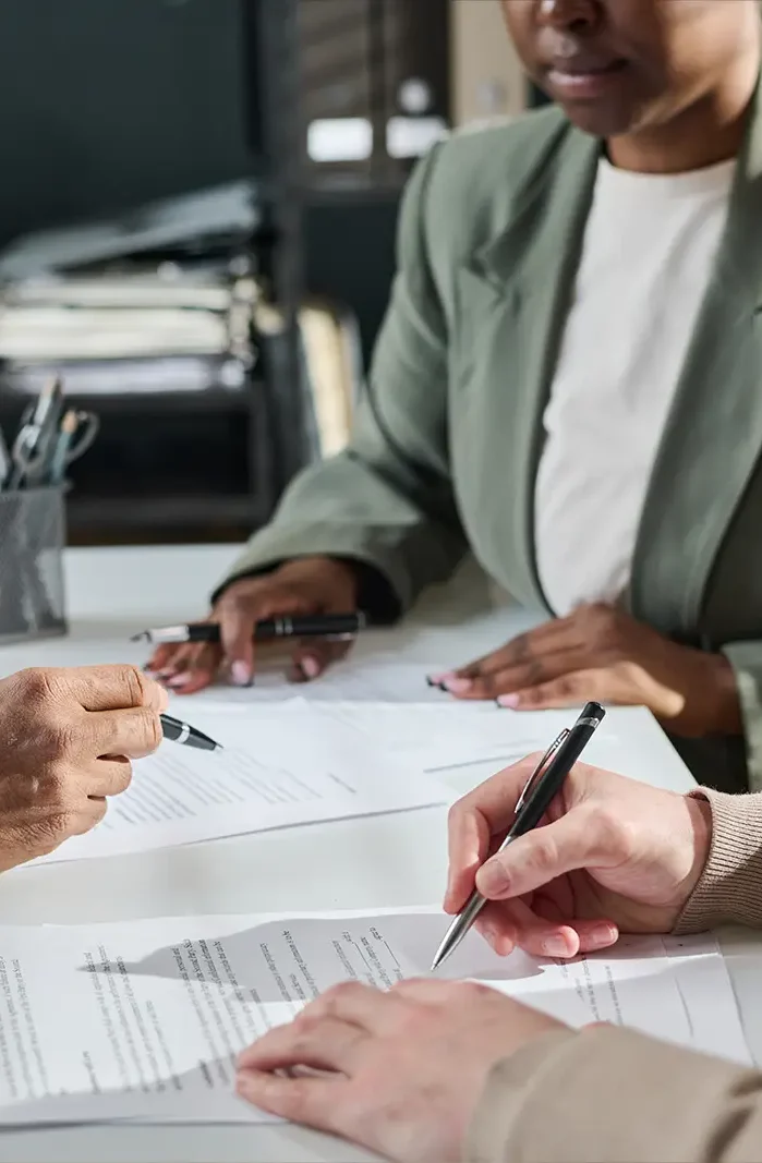 An attorney's hand points at a specific clause with his pen while two clients watch